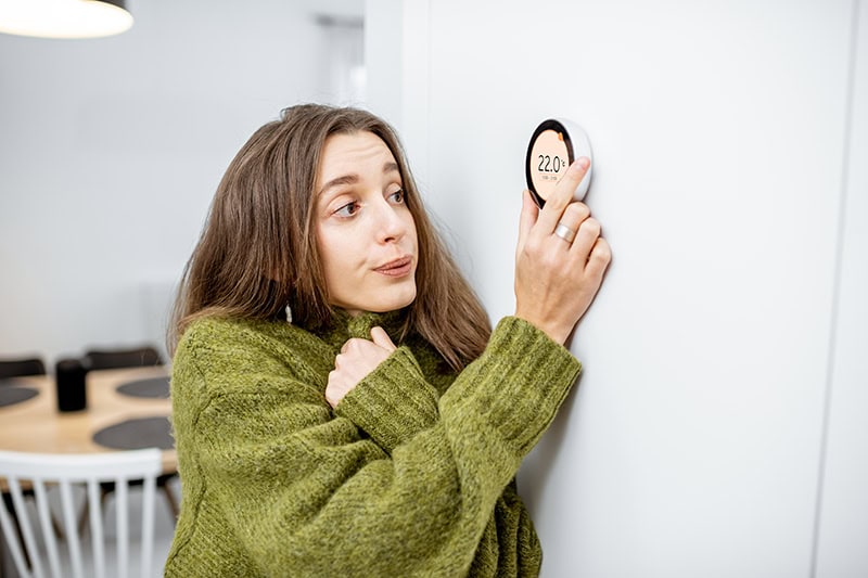 Why Is My Heat Pump Turning On and Off Frequently? A young woman changing the temperature with the thermostat.